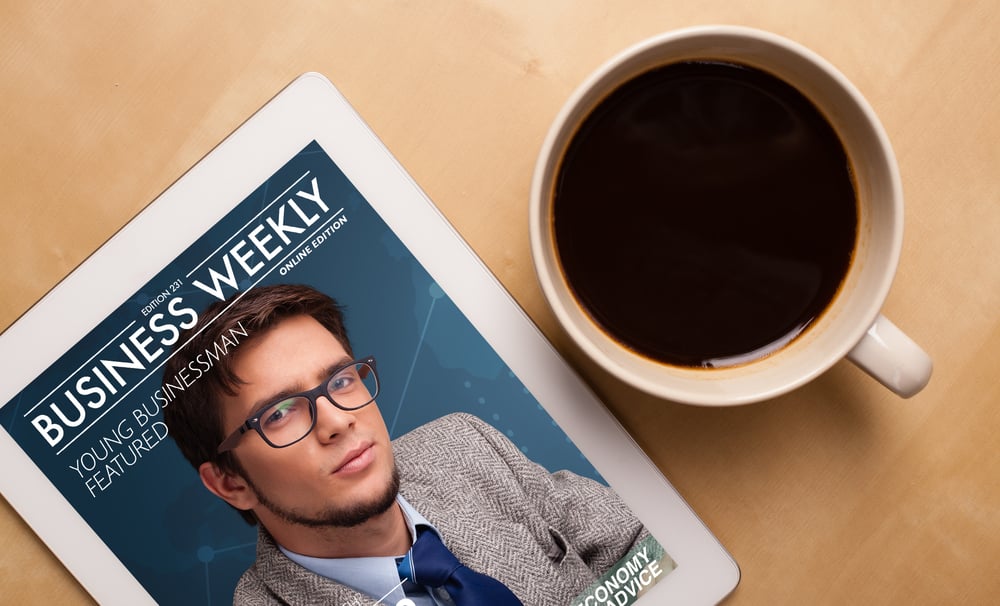 Workplace with tablet pc showing magazine cover and a cup of coffee on a wooden work table close-up
